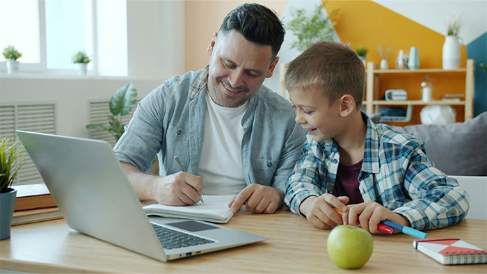 Father and son smiling while writing baby names in a notebook, researching baby names parents regret giving to kids.