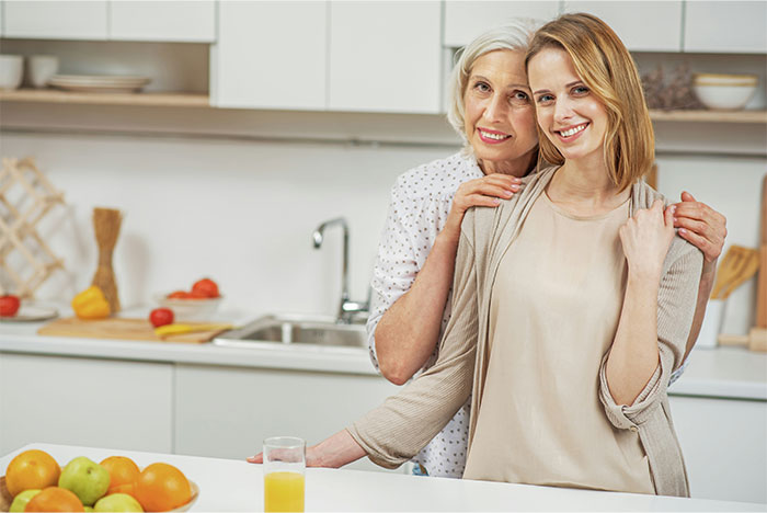 Two women smiling and embracing in a bright modern kitchen, reflecting on baby names parents regret choosing.