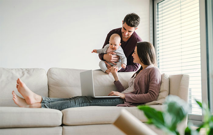Young parents with baby using a laptop on the couch, reflecting on baby names they regret giving their kids.