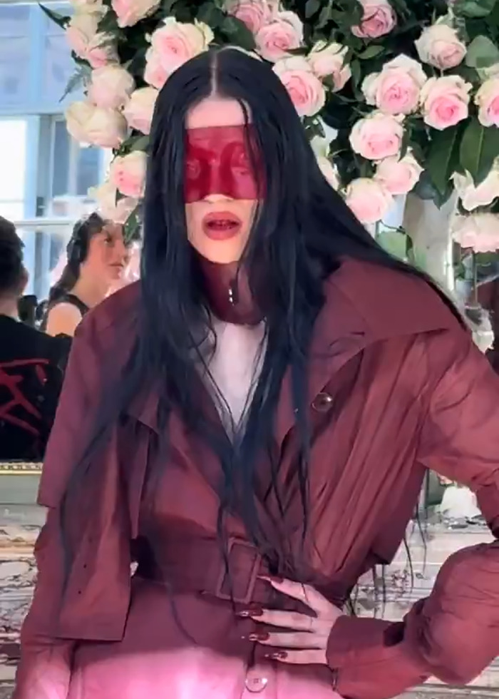 Model with long black hair wearing a red face mask and oversized jacket at Paris Fashion Week boundary-breaking show.