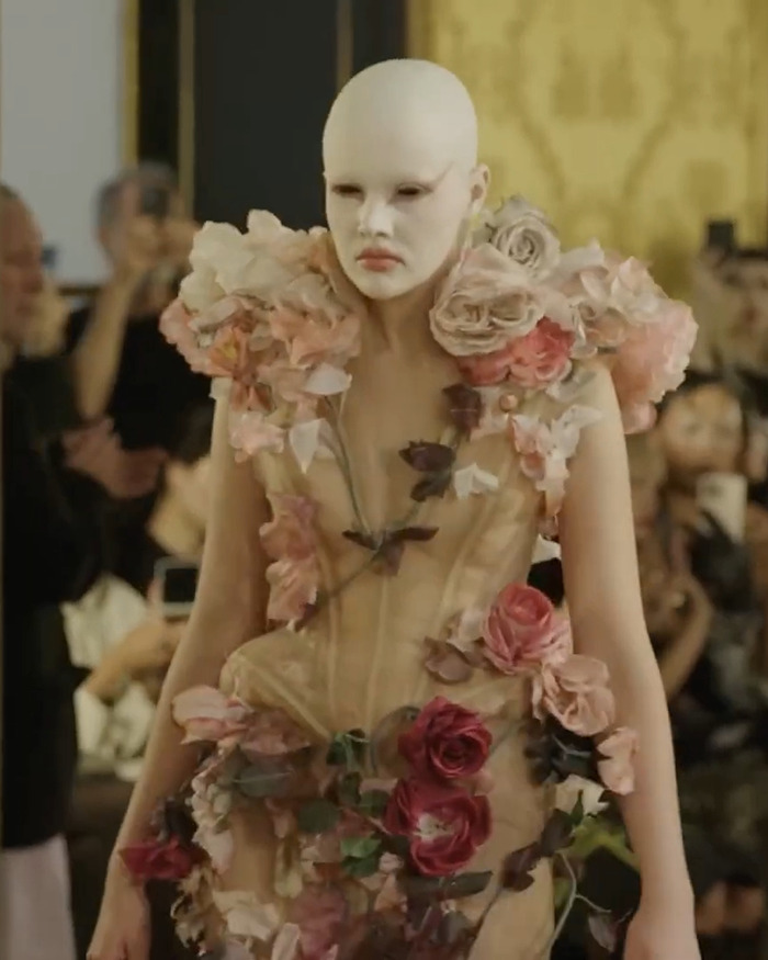 Model with white face paint wearing floral avant-garde dress at a boundary-breaking Paris Fashion Week show inspired by Hunger Games.