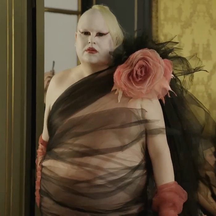 Model wearing avant-garde sheer black fabric with large pink flower at Paris Fashion Week stirring Hunger Games buzz.