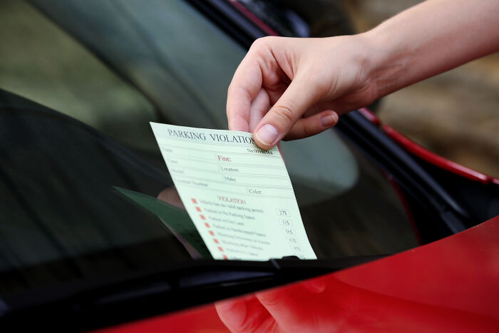 Hand placing a parking violation ticket under the windshield wiper of a red car, illustrating common loopholes to use.