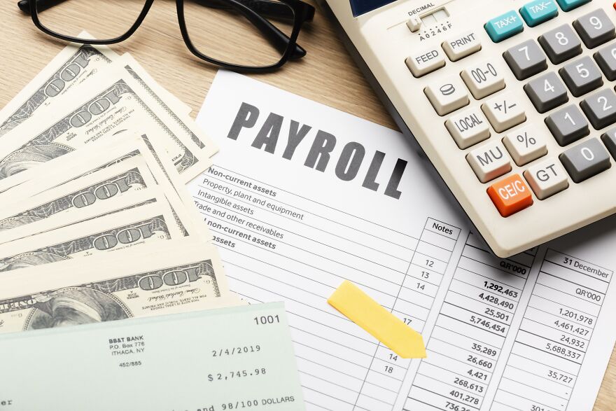 Payroll documents with cash, a paycheck, glasses, and a calculator representing no tax on overtime benefits.
