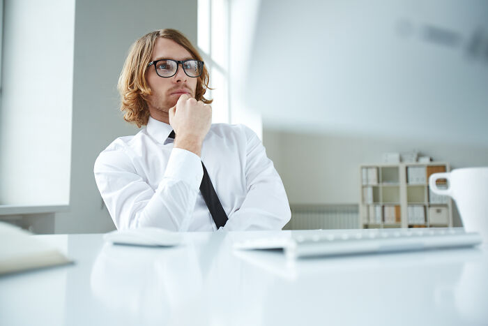 Young man with glasses and long hair sitting at a desk, deep in thought about mysteries that once baffled the world now solved
