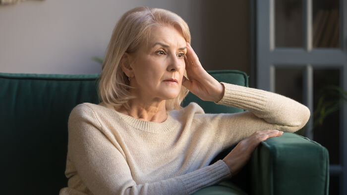 Older woman sitting on a sofa looking concerned, reflecting on strange 911 calls operators received that were true.