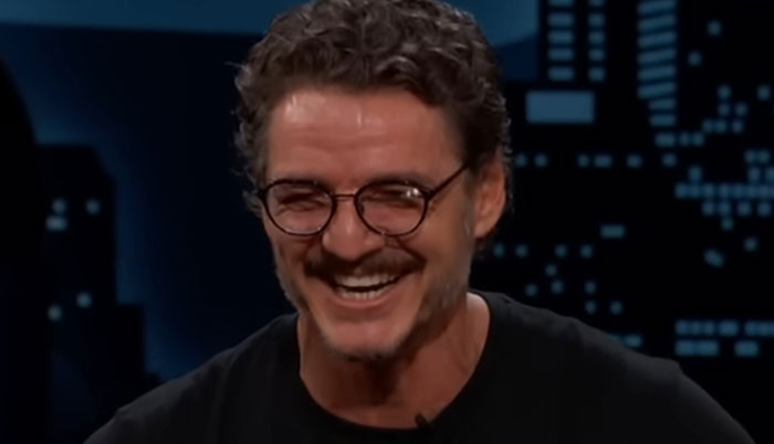 Man with curly hair and glasses smiling during a nighttime interview, sharing encounters with celebrities.