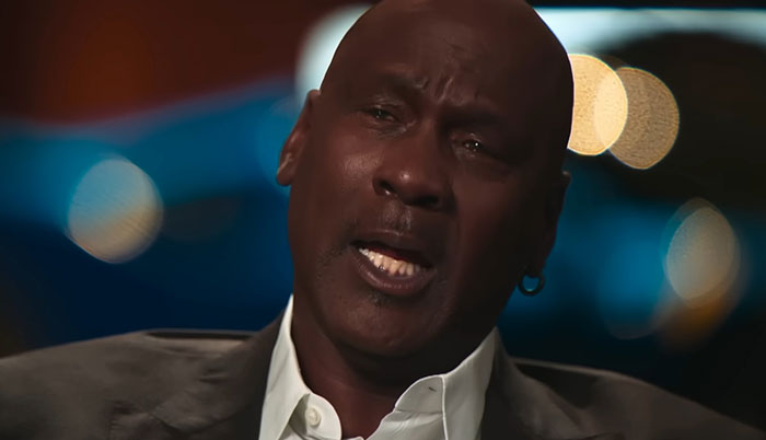 Close-up of a man sharing celebrity encounters in an interview setting with blurred lights in the background.