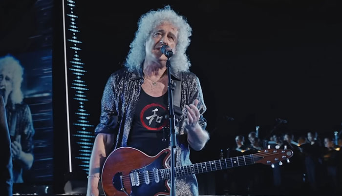 Musician with curly gray hair playing guitar and singing on stage during a live encounter with celebrities event.