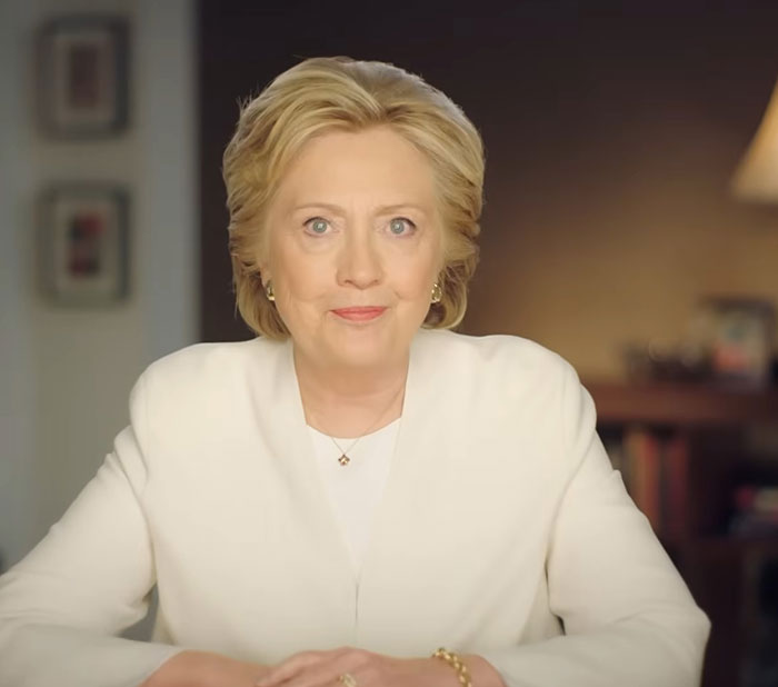 Woman in a white blazer sitting at a table, sharing celebrity encounters in a warmly lit indoor setting.