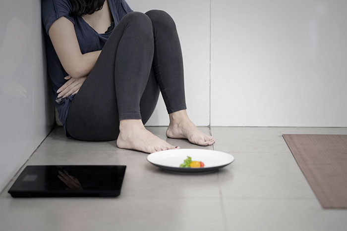 A woman sitting on the floor with bare feet by a small plate of food and a tablet, reflecting on life mistakes.