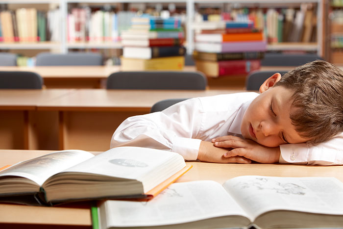 Young boy sleeping on a desk surrounded by open books, illustrating stories on how to ruin your entire life.