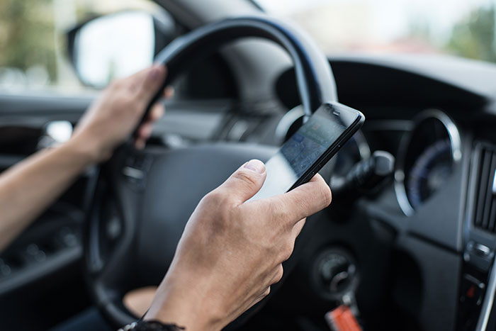 Person texting on phone while driving a car, illustrating risky behavior that can ruin your life with real consequences.