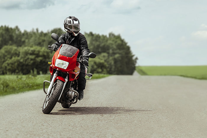 A person riding a red motorcycle on a rural road, illustrating how to ruin your entire life with risky choices.