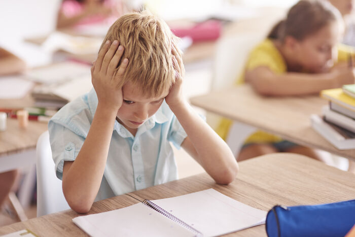Young boy in classroom holding his head, reflecting on childhood moments that still cause cringe today.