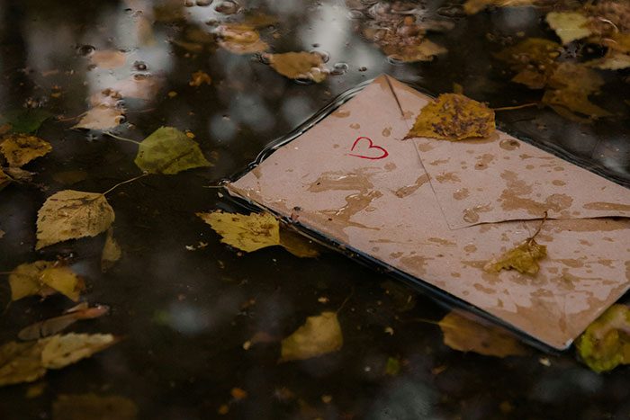 Envelope with a red heart symbol soaked in water among fallen autumn leaves, evoking creepy Halloween vibes.