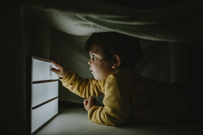 Child in a dark room touching an illuminated lightbox, evoking a creepy atmosphere perfect for true scary stories this Halloween.