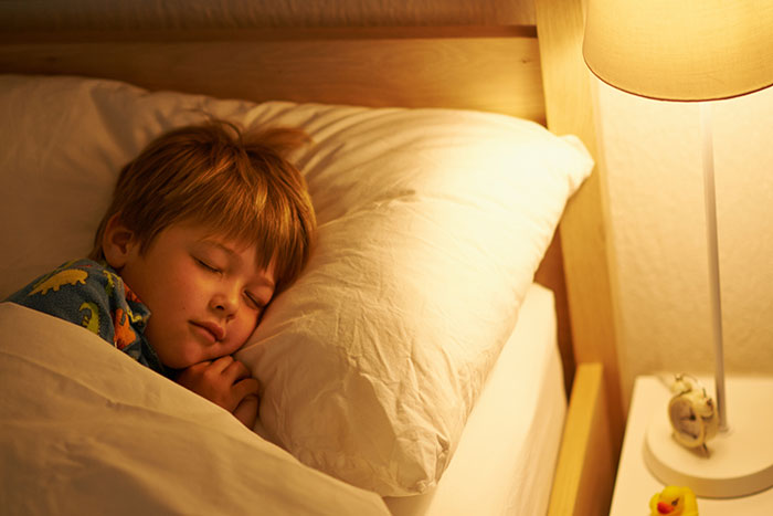Young child sleeping in bed with soft lighting, evoking the creepy true stories to keep you awake on Halloween night.