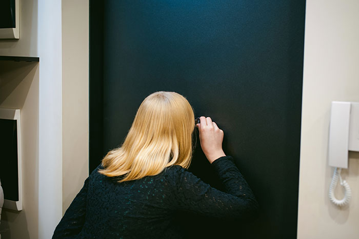 Woman with blonde hair in black dress peeking through a peephole in a dark door, evoking creepy true stories themes.