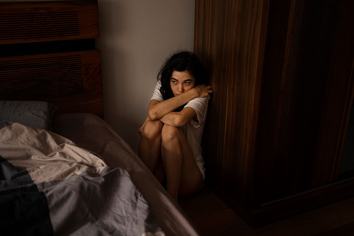 Woman sitting on floor in a dark room looking scared, illustrating creepy true stories that make you sleep with lights on.