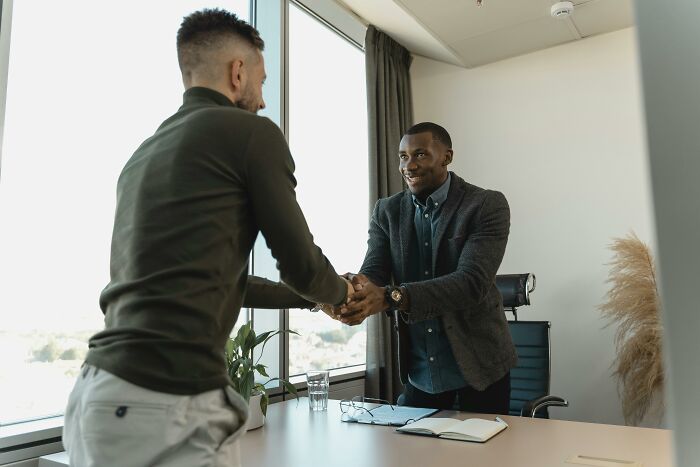Two men shaking hands in office setting, illustrating life hacks for better personal and professional connections.