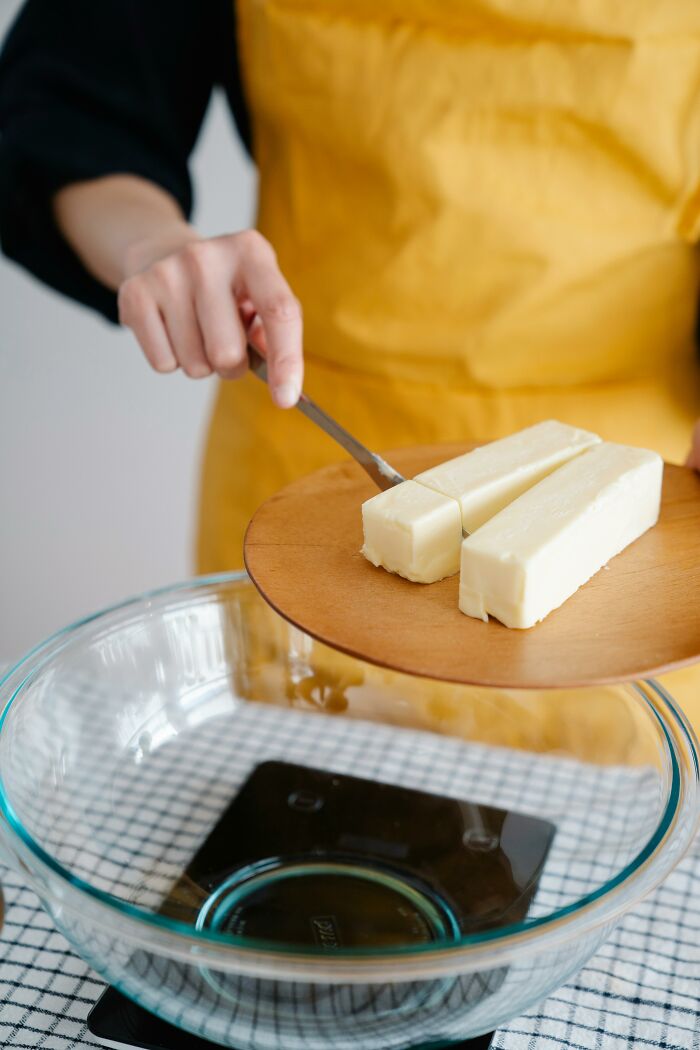 Person in yellow apron cutting butter over a glass bowl, illustrating useful life hacks for cooking and kitchen efficiency.