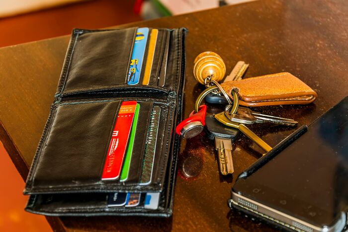Black leather wallet with credit cards next to a set of keys and a smartphone on a wooden table, showcasing life hacks.