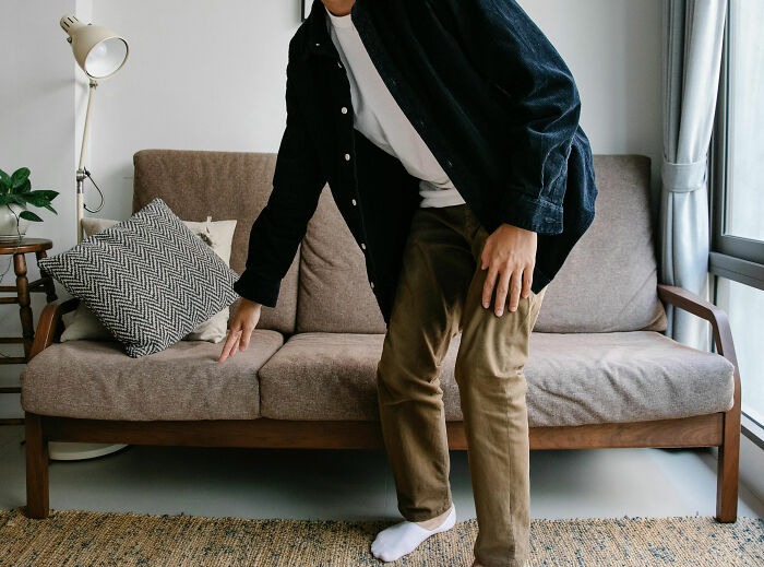 Person demonstrating a life hack by adjusting cushions on a sofa in a cozy living room setting.