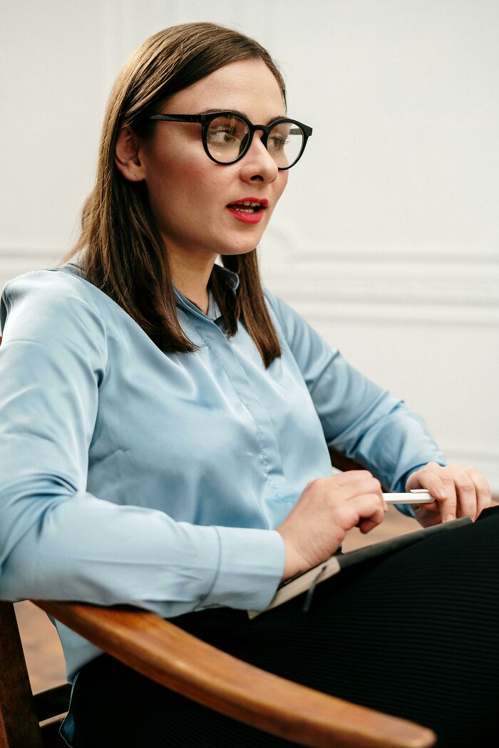 Young healthcare worker wearing glasses and a blue blouse, sitting in a chair and holding a pen during a discussion