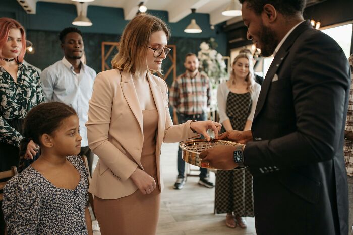 A woman receiving communion from a man in a suit, surrounded by people in a modern indoor setting.