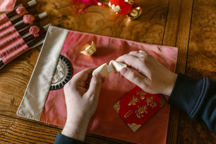 Hands breaking open a fortune cookie on a wooden table with festive Asian-themed decorations nearby.