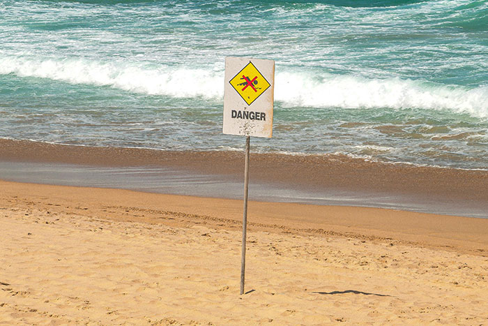 Danger sign on sandy beach with waves crashing, illustrating nightmare situations people survived against odds.