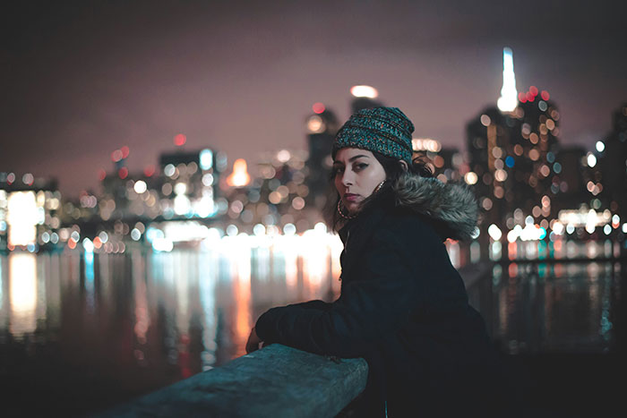 Young woman in a winter hat overlooking a city at night, evoking mood of nightmare situations people survived.