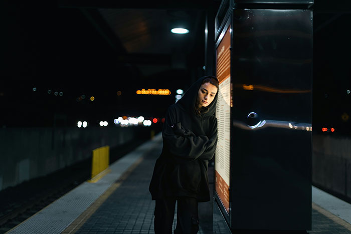Person in a dark hoodie standing alone at a dimly lit train station platform, evoking nightmare survival situations.