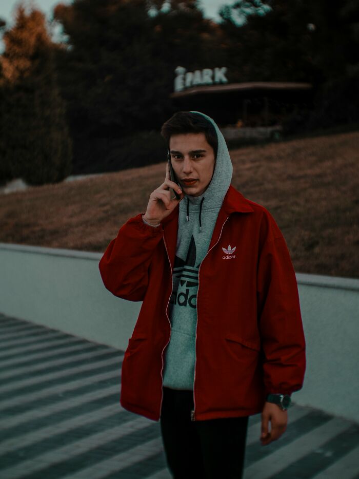 Teen in a red jacket and gray hoodie talking on a phone outdoors, reflecting on childhood rules that impact mental health.