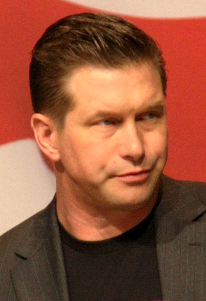 Man in a dark blazer with slicked-back hair, showing a serious expression during a celebrity encounter event.
