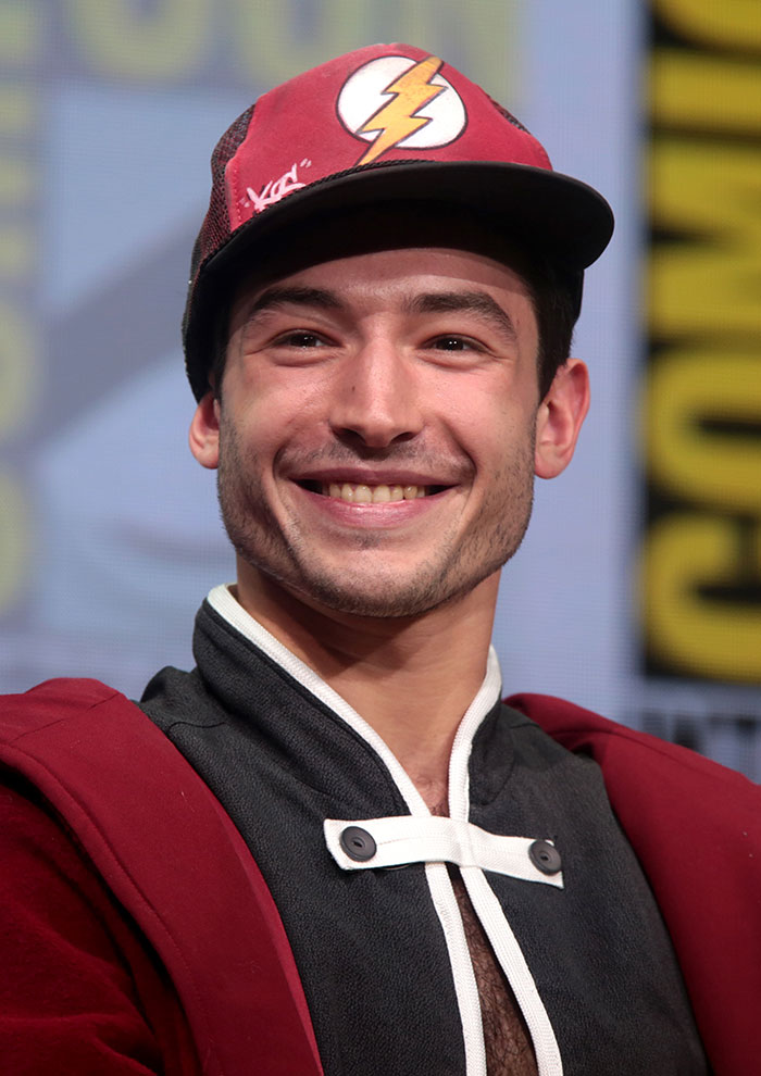 Young man smiling at a public event, wearing a red cap with a lightning bolt, related to celebrity encounters horror stories.