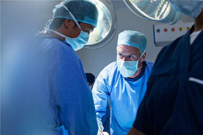 Surgeons in an operating room wearing masks and scrubs, focused on a patient during surgery and anesthesia.