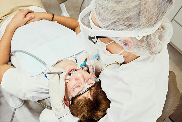 Patient receiving dental surgery, attended by a healthcare professional in protective gear during a medical procedure.