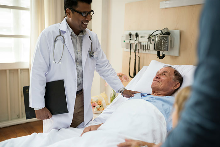 Doctor in a white coat comforting an elderly male patient in bed, relating to surgery and unexpected waking experiences.