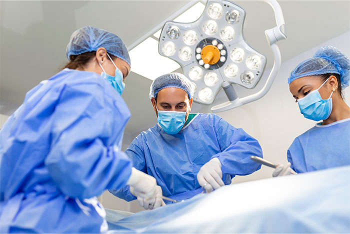 Three surgeons wearing masks and scrubs performing surgery under an operating room light during a medical procedure.