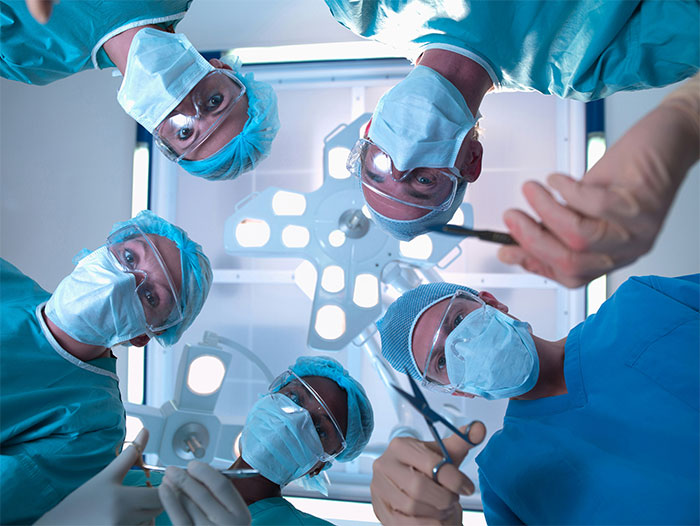 Surgeons in masks and scrubs looking down during surgery, illustrating bone-chilling and hilarious surgery stories.