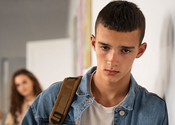 Teen boy looking regretful and isolated indoors, illustrating how to ruin your entire life through real stories online.