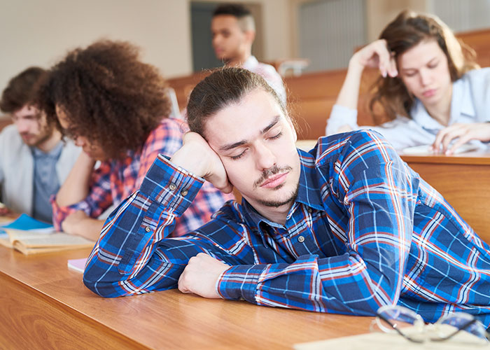 A young man looking frustrated and tired in a classroom, illustrating how to ruin your entire life concept.