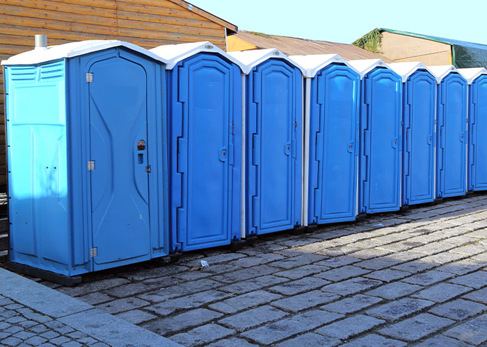 A row of blue portable toilets lined up outdoors, illustrating examples of how to ruin your entire life.