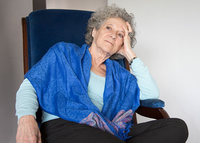 Older woman sitting in a chair looking reflective and stressed, illustrating how to ruin your entire life concept.