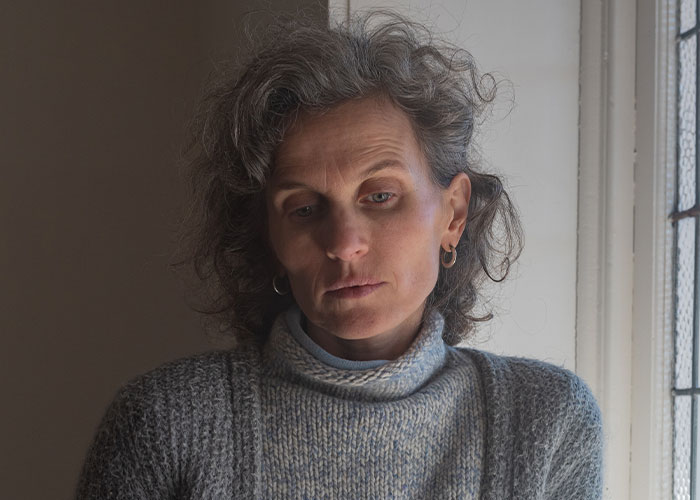 Woman in a grey sweater looking down pensively by a window, reflecting the theme of how to ruin your life stories online.