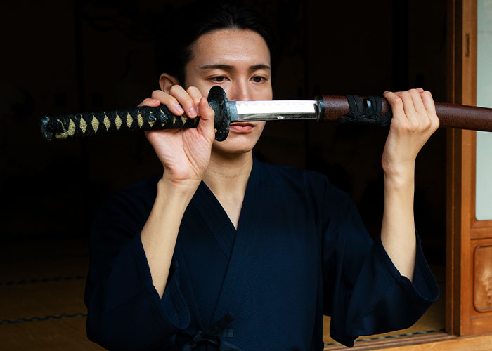 Person in traditional attire carefully examining a katana sword, symbolizing focus and reflection on how to ruin your life.