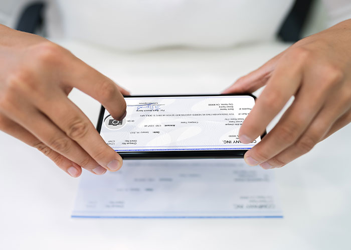 Person capturing a check image with smartphone, illustrating risk of how to ruin your entire life through financial mistakes.