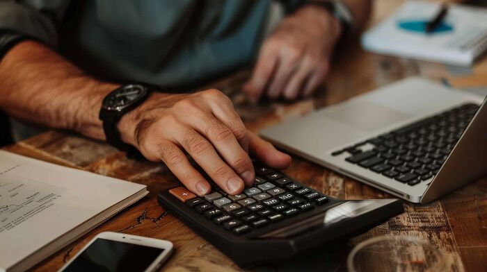 Accountant using a calculator and laptop at a wooden desk, demonstrating the dynamic side of accounting work.